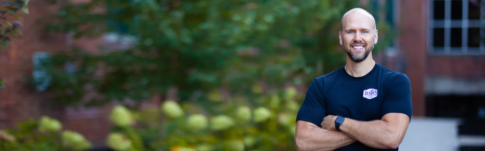 Slade Robbins, owner of Slade's Plumbing, standing outdoors in a Slade's Plumbing t-shirt
